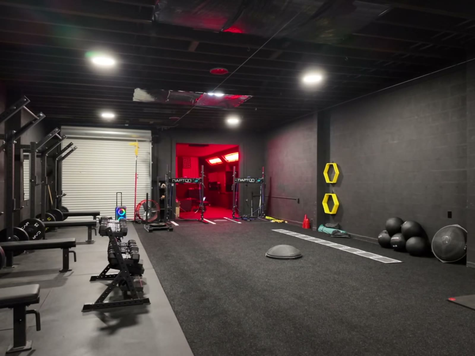 Inside Level Up in San Mateo: squat racks and benches, black turf down the middle, and the red room at the far end